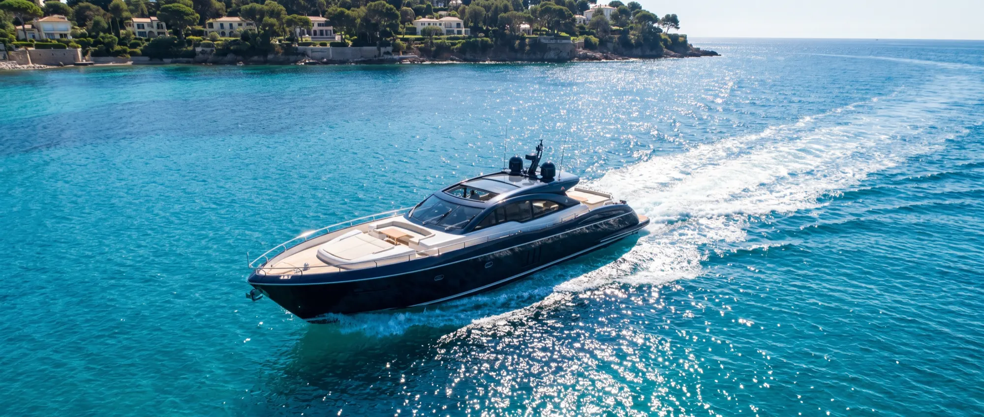 Un sport yacht bleu marine file sur une eau turquoise éclatante au large de la Côte d’Azur.