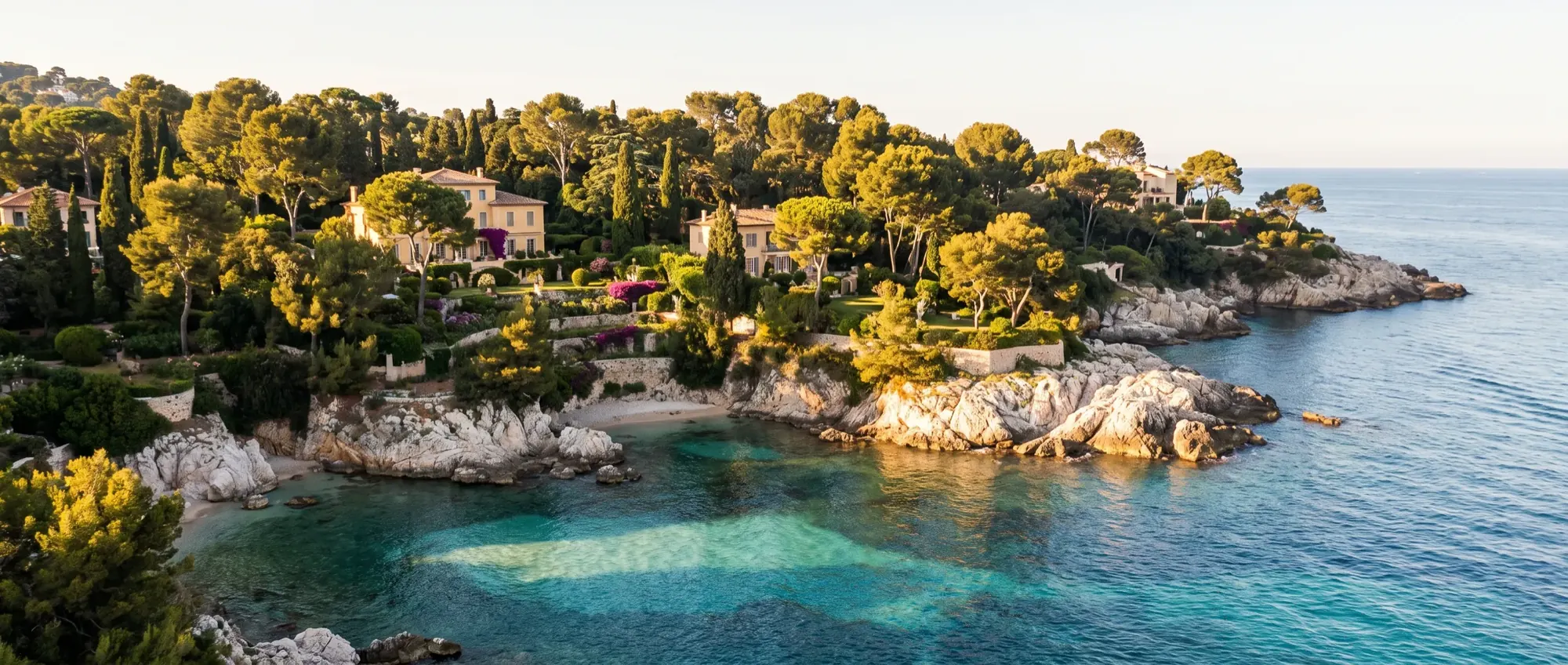 The wooded headland of Cap d’Antibes with villa gardens above a clear bay.