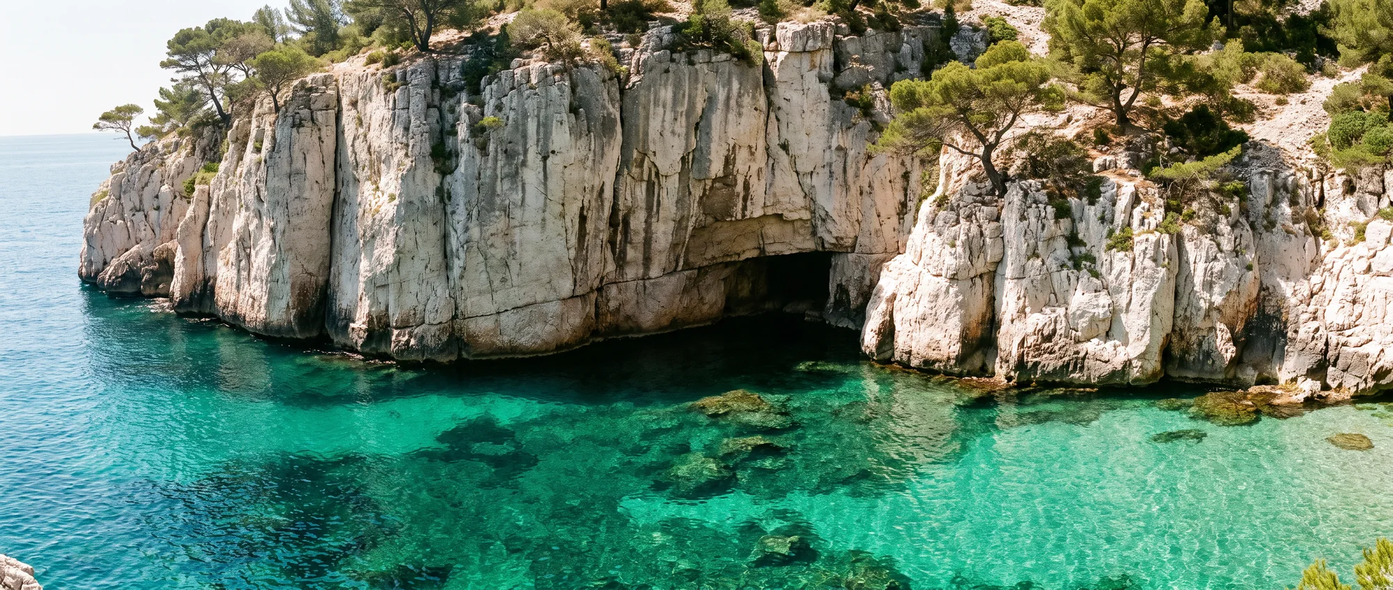Des falaises blanches plongeant droit dans une eau émeraude au fond d'une calanque.