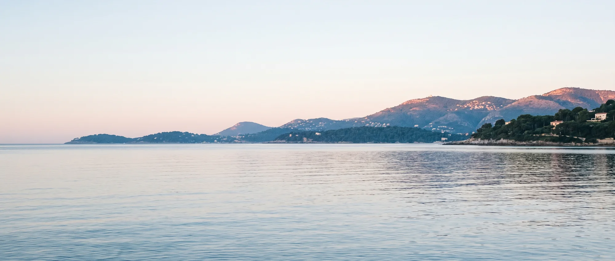 Une mer d'huile au petit matin, la côte basse et bleue derrière.
