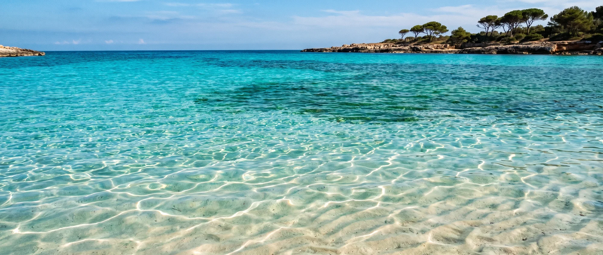 Une eau peu profonde et limpide sur le sable clair, le fond ondulant de soleil.