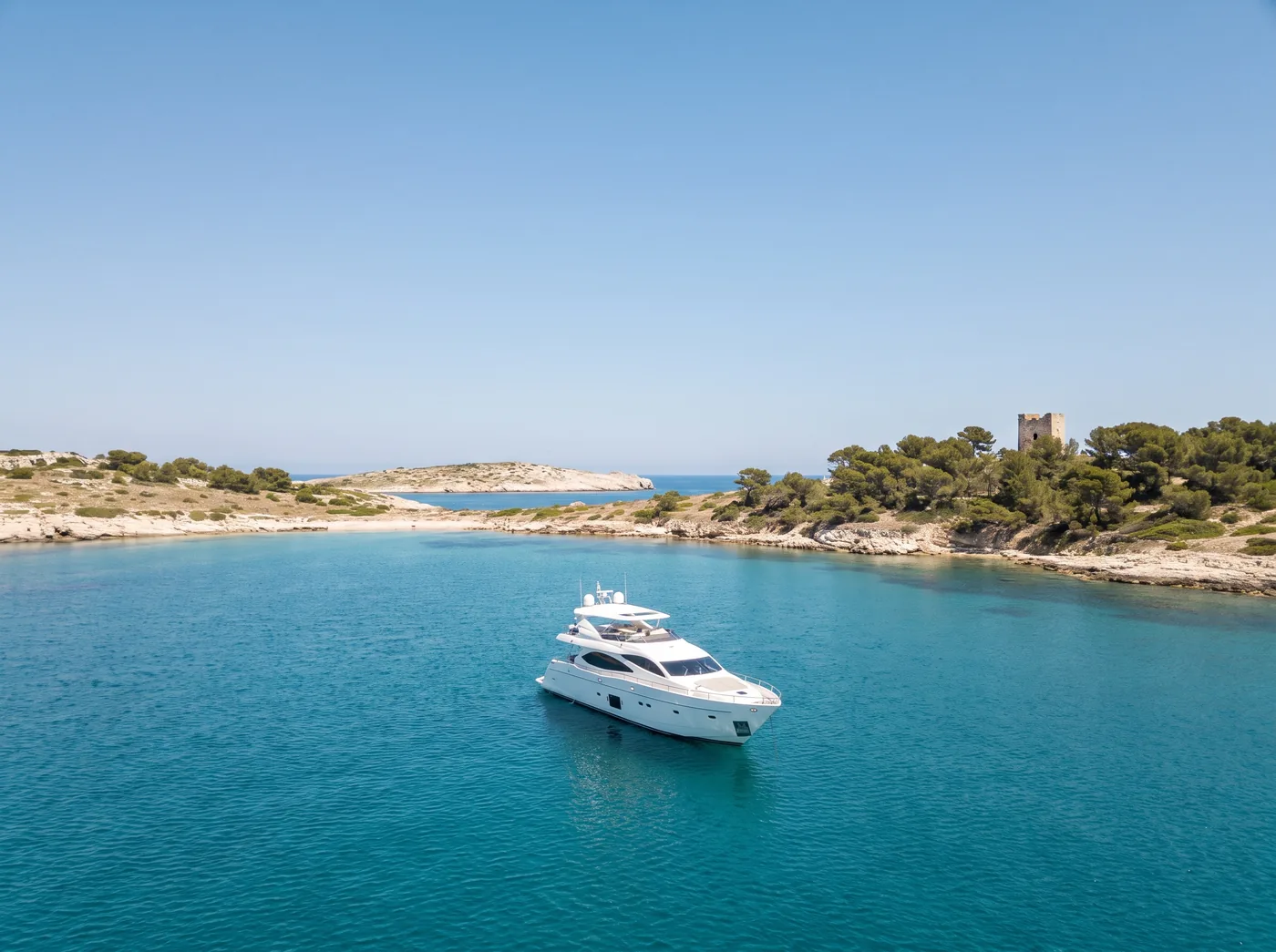 A single yacht at anchor in the wide channel between the Lérins, the old fort tower among the pines.